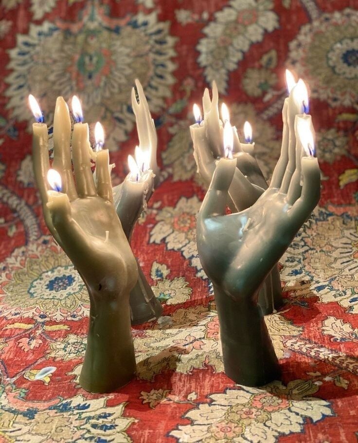 Sculptural hand-shaped candles burning over a richly patterned textile