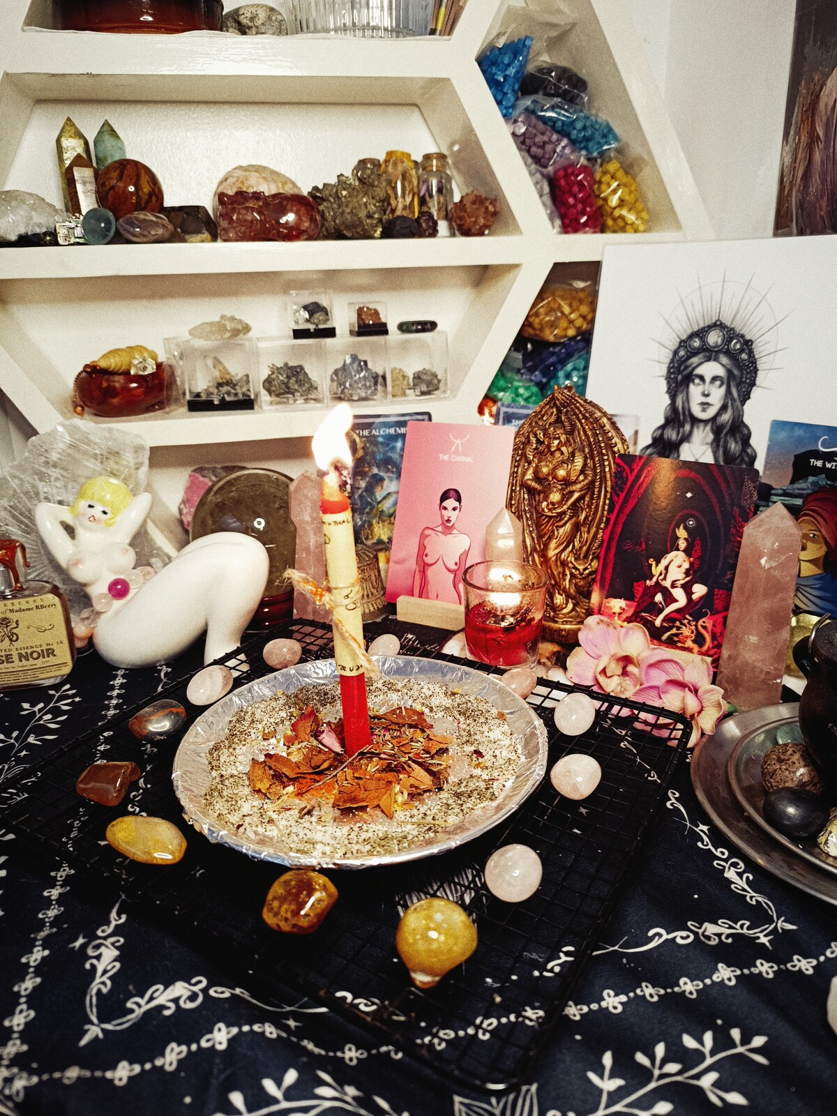 The Hot Girl X Appeal altar with a burning petition candle, rose quartz, cards, flowers, and Lilith imagery