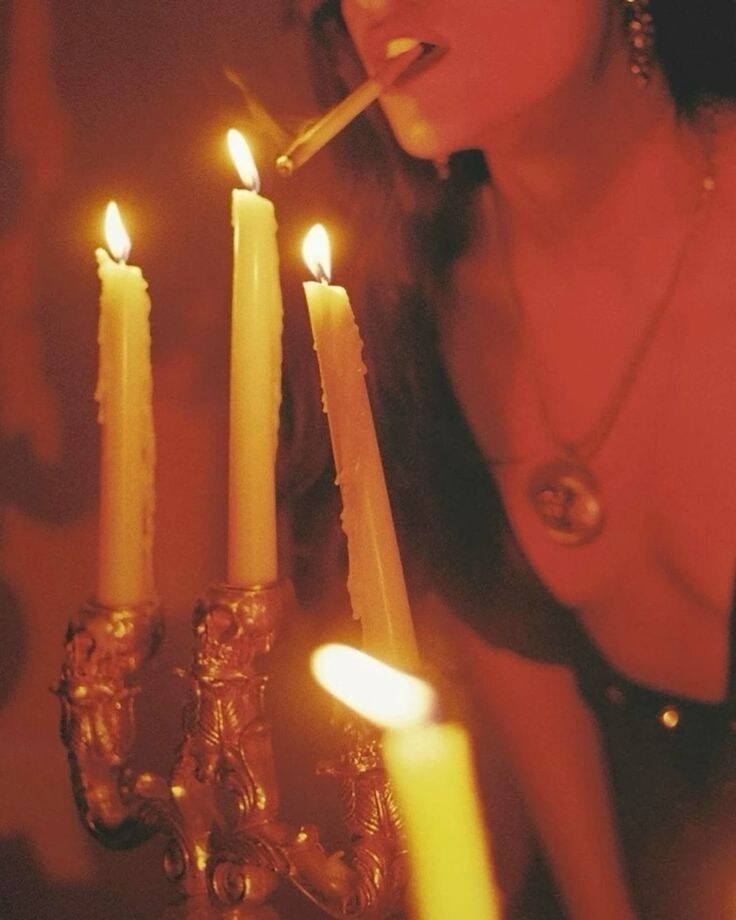 A person lighting three taper candles in warm red light