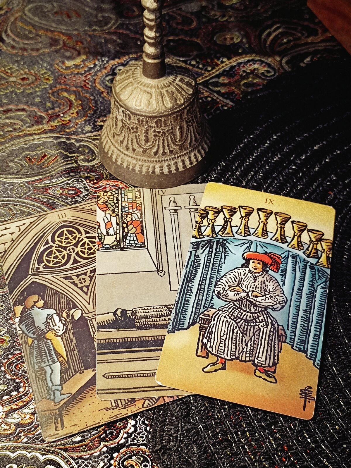 Three Tarot cards arranged beneath a brass ritual bell